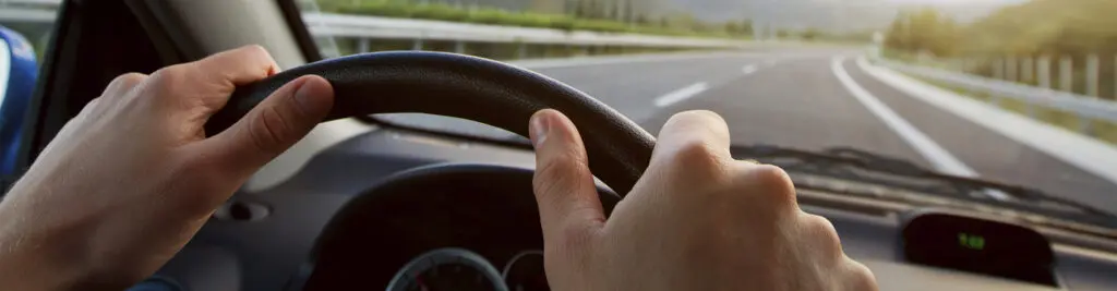 hands of a person on the starring wheel of a car, on the road